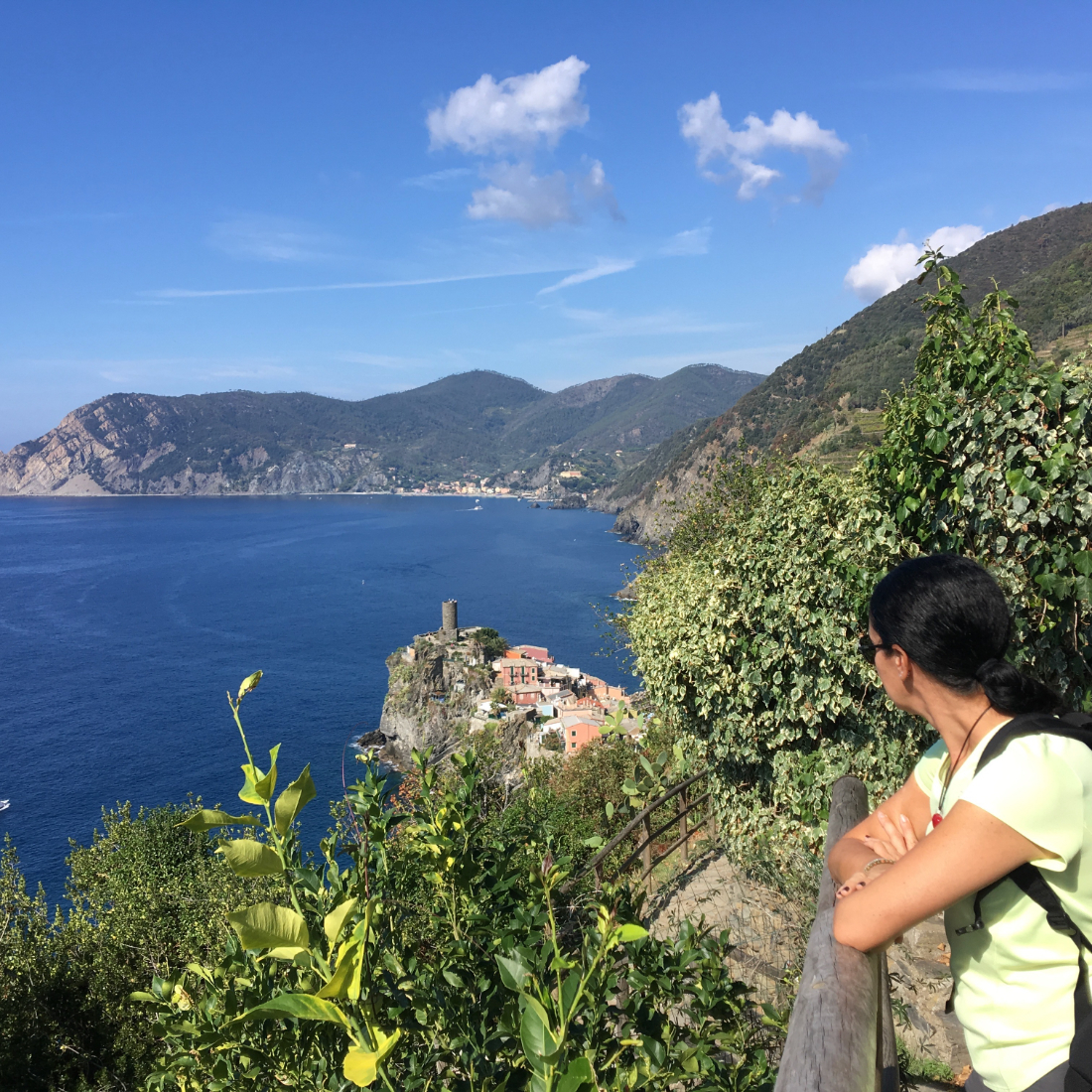 Bright blue sea and sky as a woman looks out from behind a railing along the hiking trail in Cinque Terre Italy