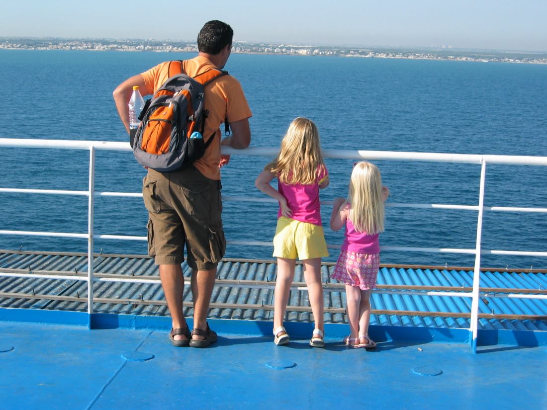 A dad and two young daughters all looking at the coastline on the horizon from a boat deck | Tips for traveling full-time with kids from Kaitlin Murray for Wanderful