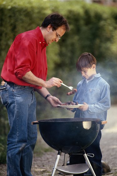 Father serving cooked food in son\'s (6-9) plate, outdoors